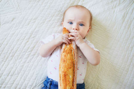 Six months old baby girl eating traditional French bread (baguette). Introducing solids to infant kids. Baby-led weaning conceptの写真素材
