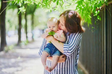Happy young woman holding her little baby girl outdoors. Mother walking with daughter on a summer dayの写真素材