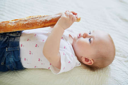 Six months old baby girl eating traditional French bread (baguette). Introducing solids to infant kids. Baby-led weaning conceptの写真素材