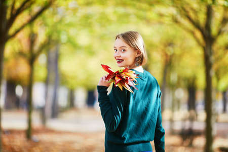 Beautiful young woman with bunch of colorful autumn leaves walking in park on a fall day. Luxembourg...