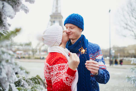 Happy couple near Christmas tree under snow with the Eiffel tower in the background on a winter day....
