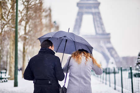 Couple of tourists walking in Paris under umbrella on a day with heavy snow. Unusual weather conditions in Parisの写真素材