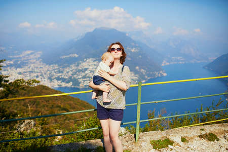 Woman with little girl enjoying scenic view to the lake Lugano from mountain San Salvatore in...