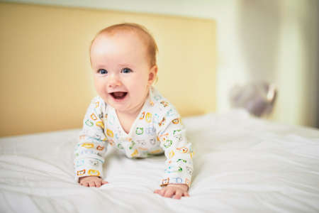 Adorable baby girl in pyjamas having fun on bed in nurseryの写真素材