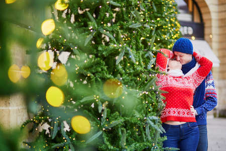 Happy couple in colorful sweaters walking on a street of Paris decorated for Christmasの写真素材