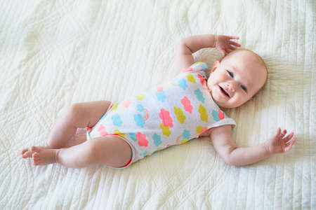 Baby girl lying on bed and smiling. Happy healthy little child laughing. Infant kid in sunny nurseryの写真素材