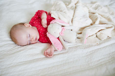 Baby girl sleeping under knitted blanket with her favorite toy. Little child in pink clothes having...