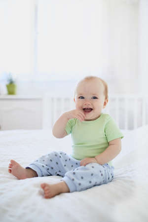 Baby girl sitting on bed and laughing. Happy healthy little child at home. Infant kid in sunny...