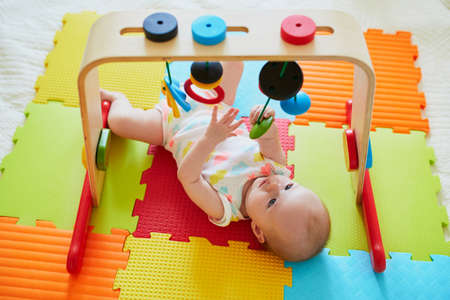 Adorable baby girl having fun with toys on colorful play mat. Happy healthy kid playing on the floor