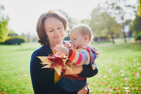 Happy smiling woman with baby girl and bunch of red maple leaves on sunny fall day in park. Autumn activities with kidsの写真素材