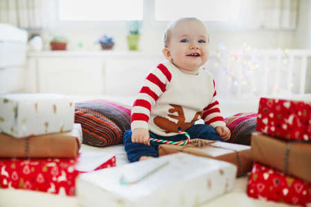 Happy little baby girl wearing warm holiday sweater opening Christmas presents on her very first Christmas. Celebrating Xmas with kids at homeの写真素材