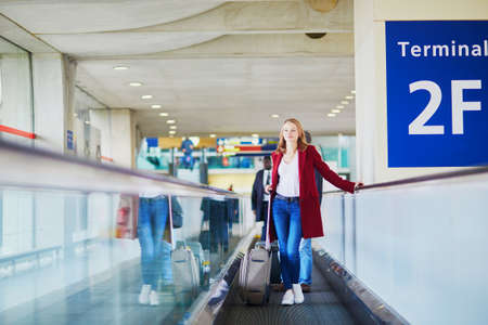 Young woman in international airport with luggage on travelatorの写真素材