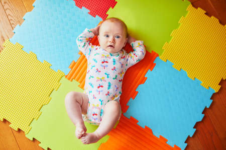 4 months old baby girl lying on colorful play mat on the floor. Activity carpet for kidsの写真素材