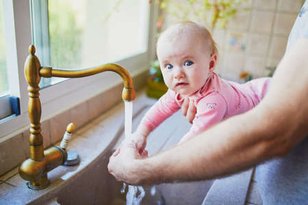 Father holding his little baby girl and helping her to wash hands