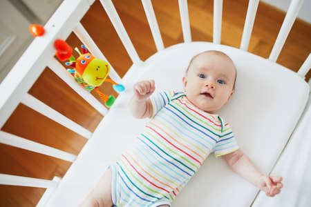 Adorable baby girl in co-sleeper crib attached to parents' bed. Little child having a day nap in cot. Infant kid in sunny nurseryの写真素材
