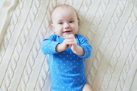 Adorable baby girl lying on bed and smiling. Happy healthy little child laughing. Infant kid in sunny nurseryの写真素材