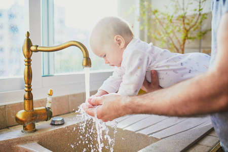 Father holding his little baby girl and helping her to wash handsの写真素材
