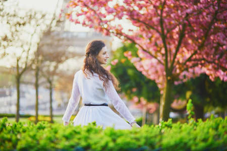 Happy young woman in white dress enjoying cherry blossom season in Paris, France