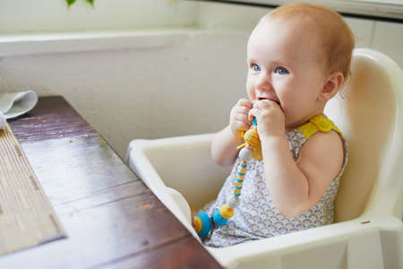 Little baby girl sitting in high chair in cafe, restaurant or at home