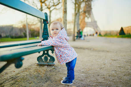 One year old girl standing next to bench near the Eiffel tower. Toddler learning how to walk. Adorable child walking in Paris, France. Traveling with kidsの写真素材