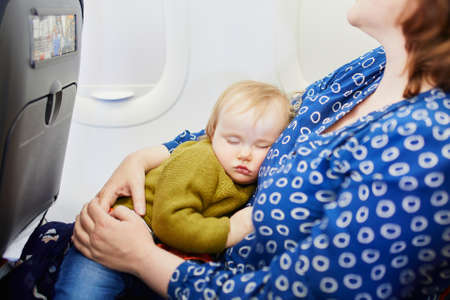 Woman with little girl travelling by plane. Mother holding her sleeping baby during the flight. Travelling with kidsの写真素材