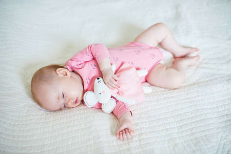 Baby girl having a nap with her favorite mouse toy. Little child sleeping on bed with comforter....