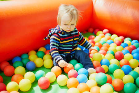 Little girl playing in ball pool. Toddler having fun with balls. Colorful toys for children.