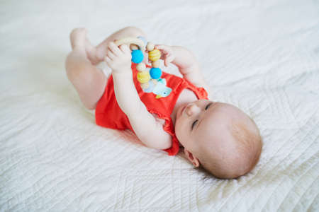 Cute baby girl lying on her back on bed. Happy healthy kid with toy in nurseryの写真素材