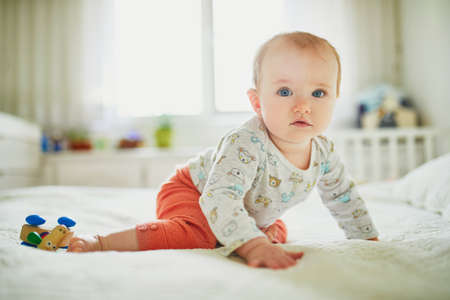 Baby girl sitting on bed. Happy healthy little child at home. Infant kid in sunny nurseryの写真素材