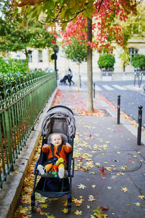 Adorable little girl in bright stylish clothes sitting in pushchair outdoors on a fall day in Paris, France. Autumn walks with kidsの写真素材
