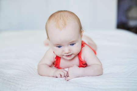 Cute baby girl lying on her tummy on bed. Happy healthy kid in nursery