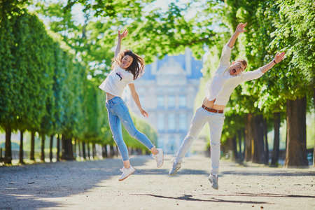 Happy romantic couple in Paris, jumping in Tuileries garden. Tourists spending their vacation in...