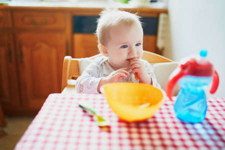 Cute baby girl eating lunch in the kitchen. Little kid tasting solids at home. Baby led weaningの写真素材