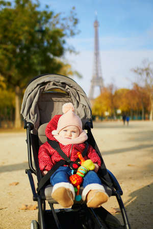 Adorable little girl in bright stylish clothes sitting in pushchair outdoors on a fall day in Paris, France. Autumn walks with kidsの写真素材