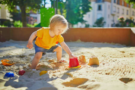 Adorable little girl on playground in sandpit. Toddler playing with sand molds and making mudpies. Outdoor creative activities for kidsの写真素材