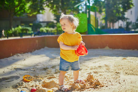 Adorable little girl on playground in sandpit. Toddler playing with sand molds and making mudpies. Outdoor creative activities for kidsの写真素材