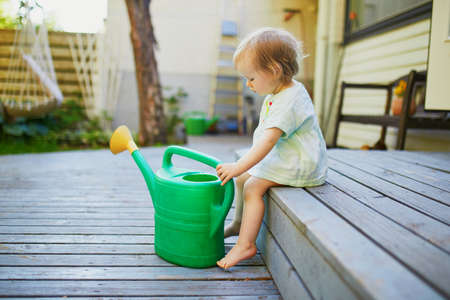 Cute baby girl playing with watering pot a warm summer day. Little kid helping parents to take care of the garden. Child with sprinkling canの写真素材
