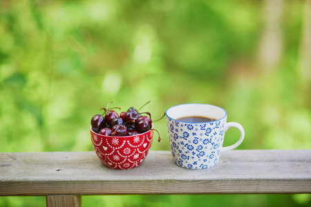 Cup of black coffee and bowl of sweet cherriesの写真素材