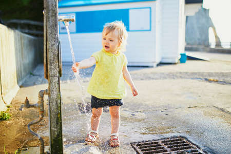 Adorable toddler girl playing with water tap outdoors. Outdoor activities for kidsの写真素材