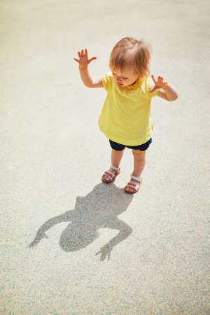Adorable toddler girl playing with her shadow on a sunny day. Little kid being brave and struggling her fearsの写真素材