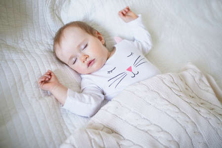 Adorable baby girl sleeping in crib under knitted blanket. Small kid having day nap in parents' bed