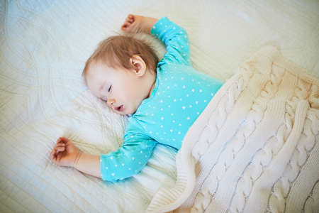 Adorable baby girl sleeping in crib under knitted blanket. Small kid having day nap in parents bedの写真素材