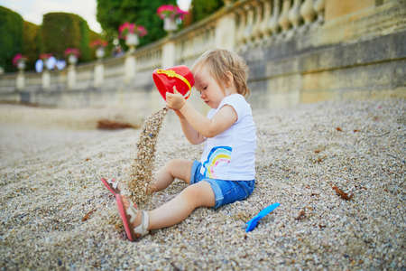 Little girl sitting on a large heap of stones and playing with pebbles in Luxembourg garden of...