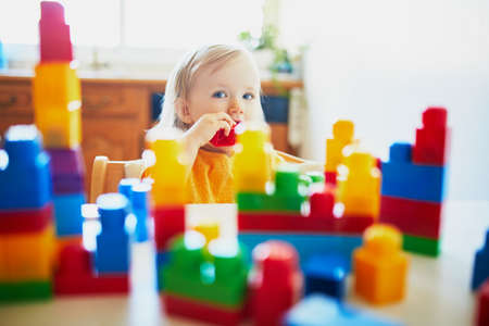Adorable little girl playing with colorful plastic construction blocks at home, in kindergaten or...