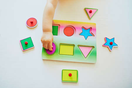 Toddler girl or boy doing wooden puzzle. Child learning geometric shapes. Kid learning to solve...