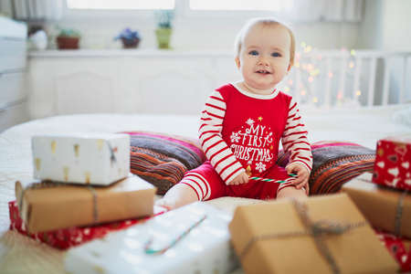 Happy little baby girl wearing pyjamas opening Christmas presents on her very first Christmas. Celebrating Xmas with kids at homeの写真素材