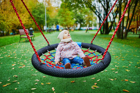 Adorable little girl on the playground. Toddler having fun on basket swing on a fall day. Outdoor activities for small kidsの写真素材