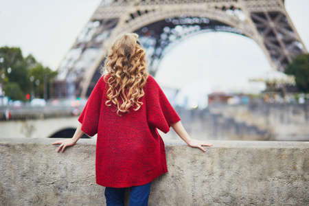 Young woman with long blond curly hair in Paris, France. Beautiful tourist in red coat near the...