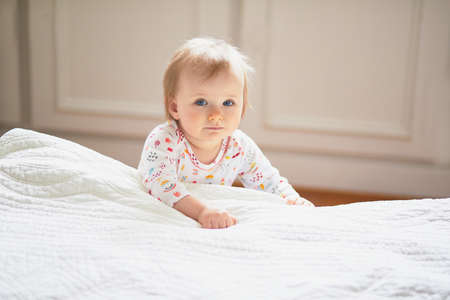 Baby girl playing near bed and laughing. Happy healthy little child at home. Infant kid in sunny...