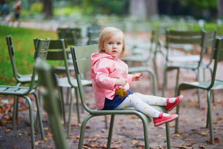 Adorable toddler girl sitting on traditional green chair in Tuileries garden in Paris, France. Happy child enjoying warm and sunny fall day. Outdoor autumn activities for kidsの写真素材